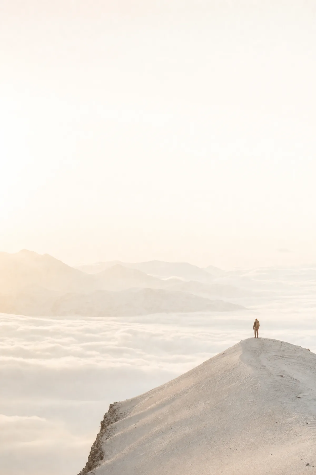 A lone figure walking a sunlit ridge above a sea of cloud at dawn